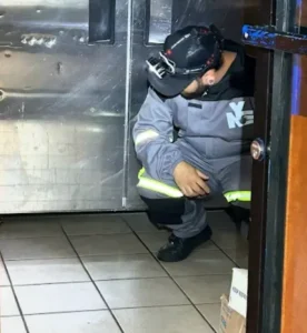 Man in grey jumpsuit with reflective stripes and a headlamp squatting near a stainless steel wall.