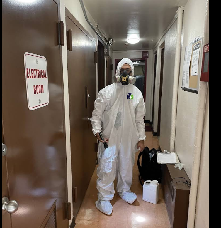 NYE technician in full PPE treating a building interior, NYC