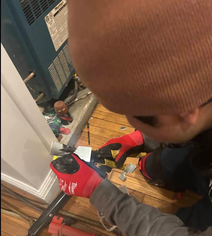 Technician custom-cutting metal to seal a rodent entry point, NYC