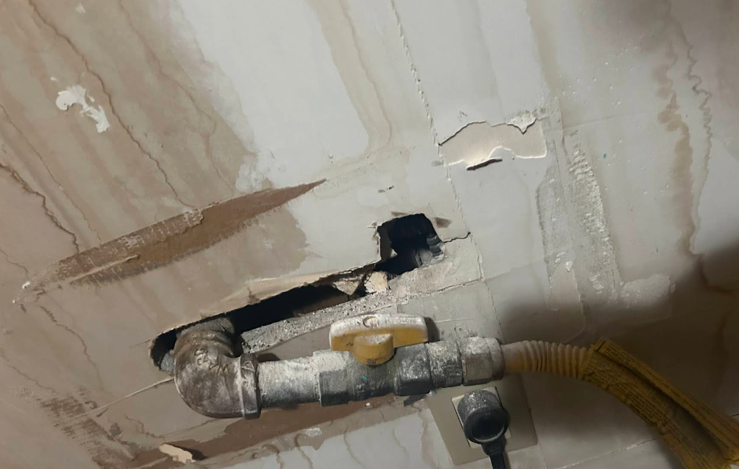 Large broken wall opening around a gas line before sealing, NYC