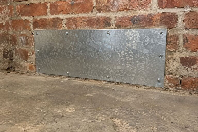 Galvanized sheet metal patch screwed over a hole in a basement brick wall