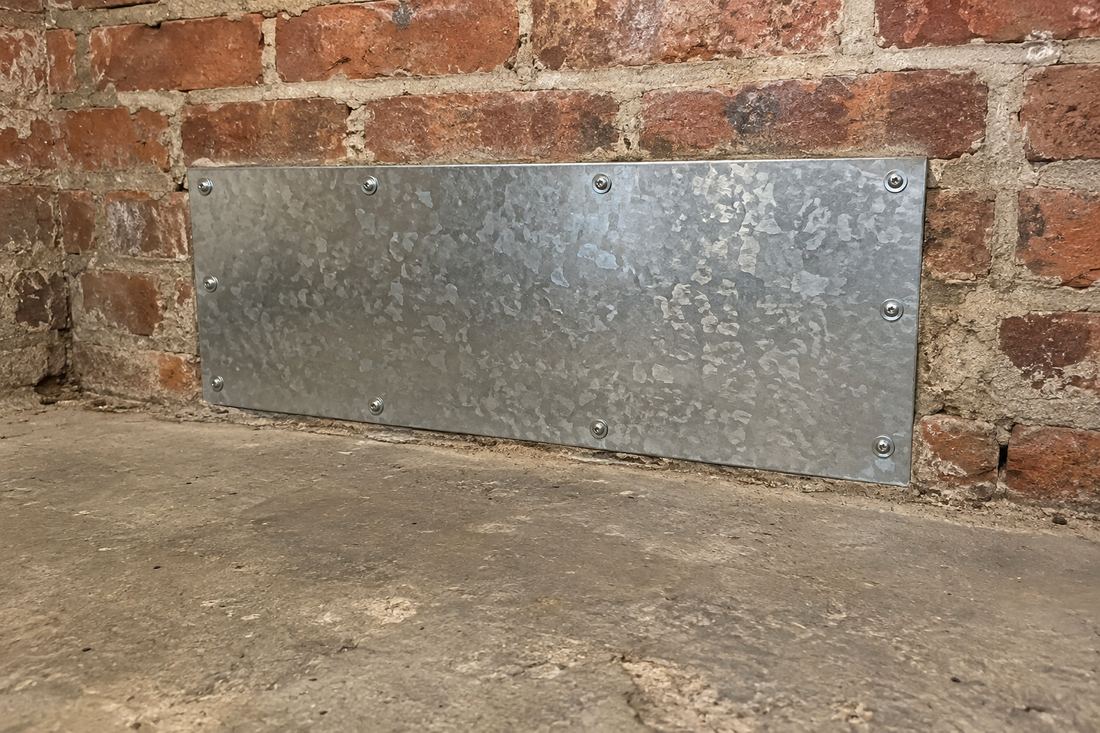 Galvanized sheet metal patch screwed over a hole in a basement brick wall