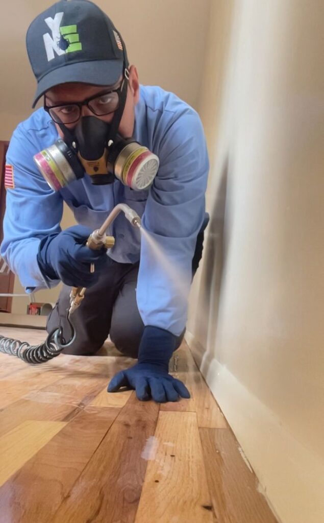 NYE technician applying a crack-and-crevice treatment along a baseboard