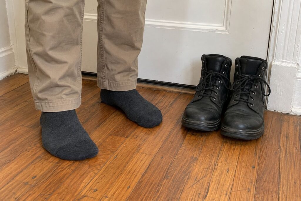 NYE technician in clean socks with work boots placed neatly by an apartment door