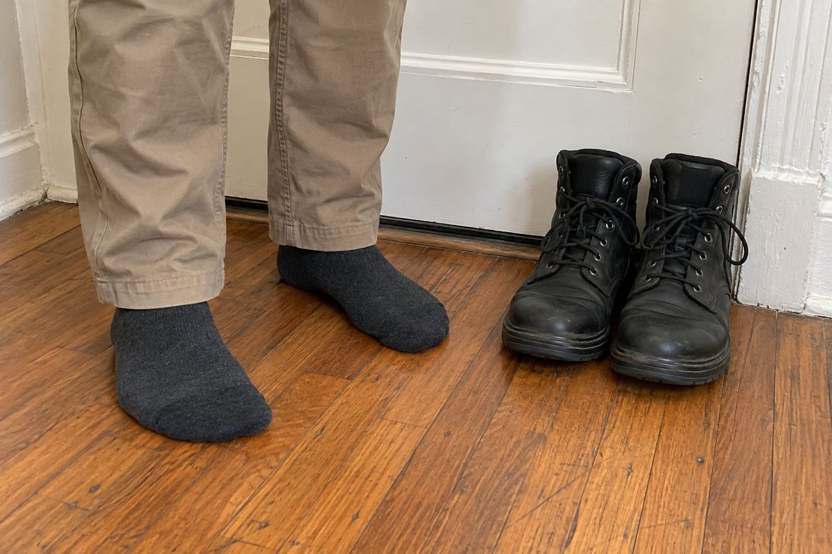 NYE technician in clean socks with work boots placed neatly by an apartment door