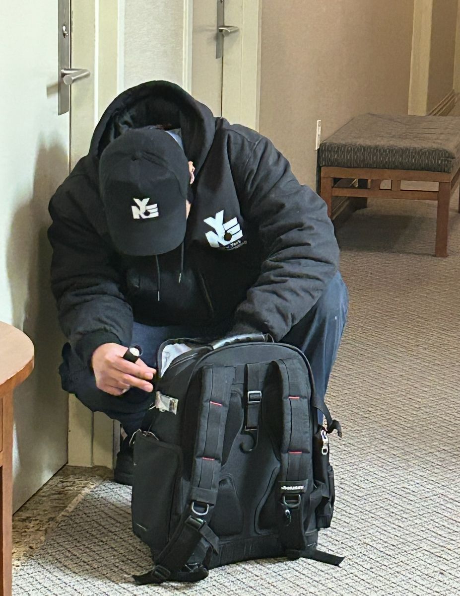 NYE technician in company cap and jacket preparing equipment in an NYC apartment building hallway
