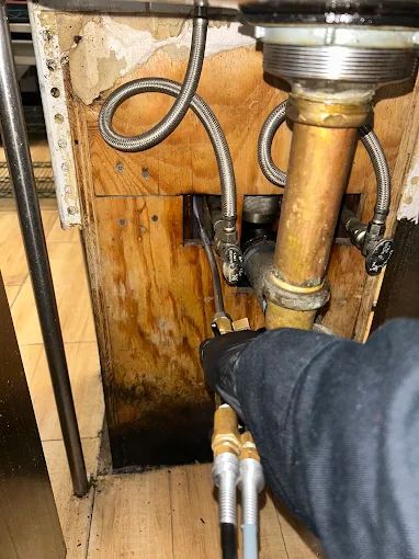 NYE technician micro-injecting into the wall void around plumbing under a sink